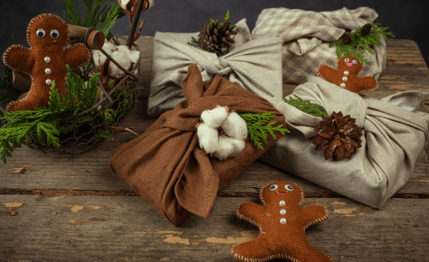 Fabric-wrapped gifts with pinecones and greenery, alongside felt gingerbread ornaments, showcasing an Eco-Friendly Gift-Giving approach.