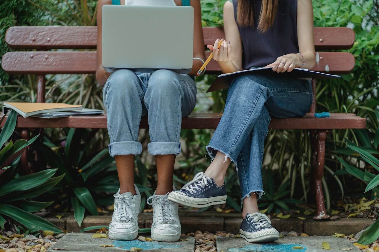 Two students studying outdoors on a bench with a laptop and notebook, practicing sustainable living for students by utilizing natural surroundings for study sessions.