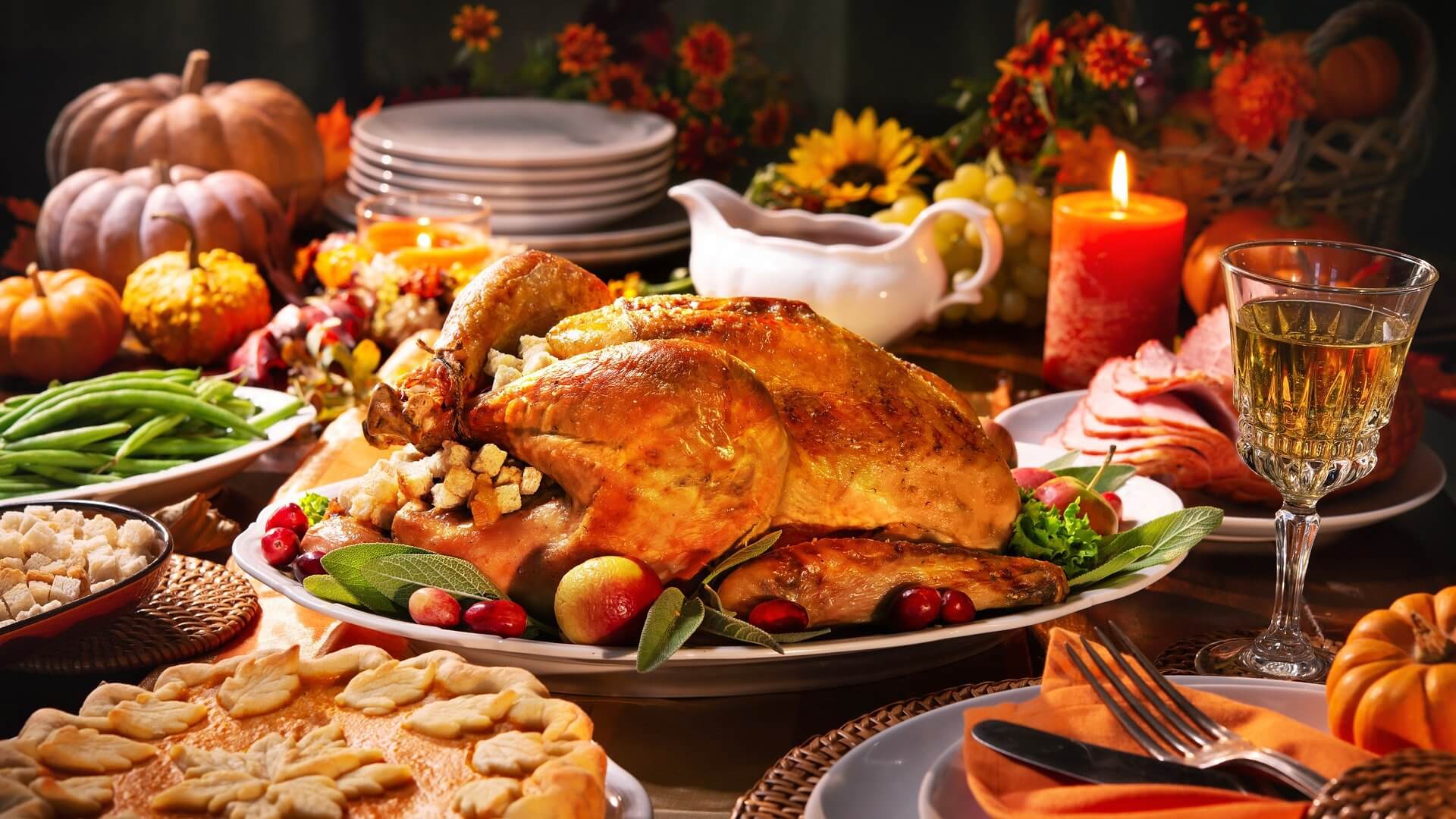 Sustainable Thanksgiving dinner table with a roasted turkey centerpiece, side dishes of green beans and ham, pie, and festive fall decorations including pumpkins and candles.